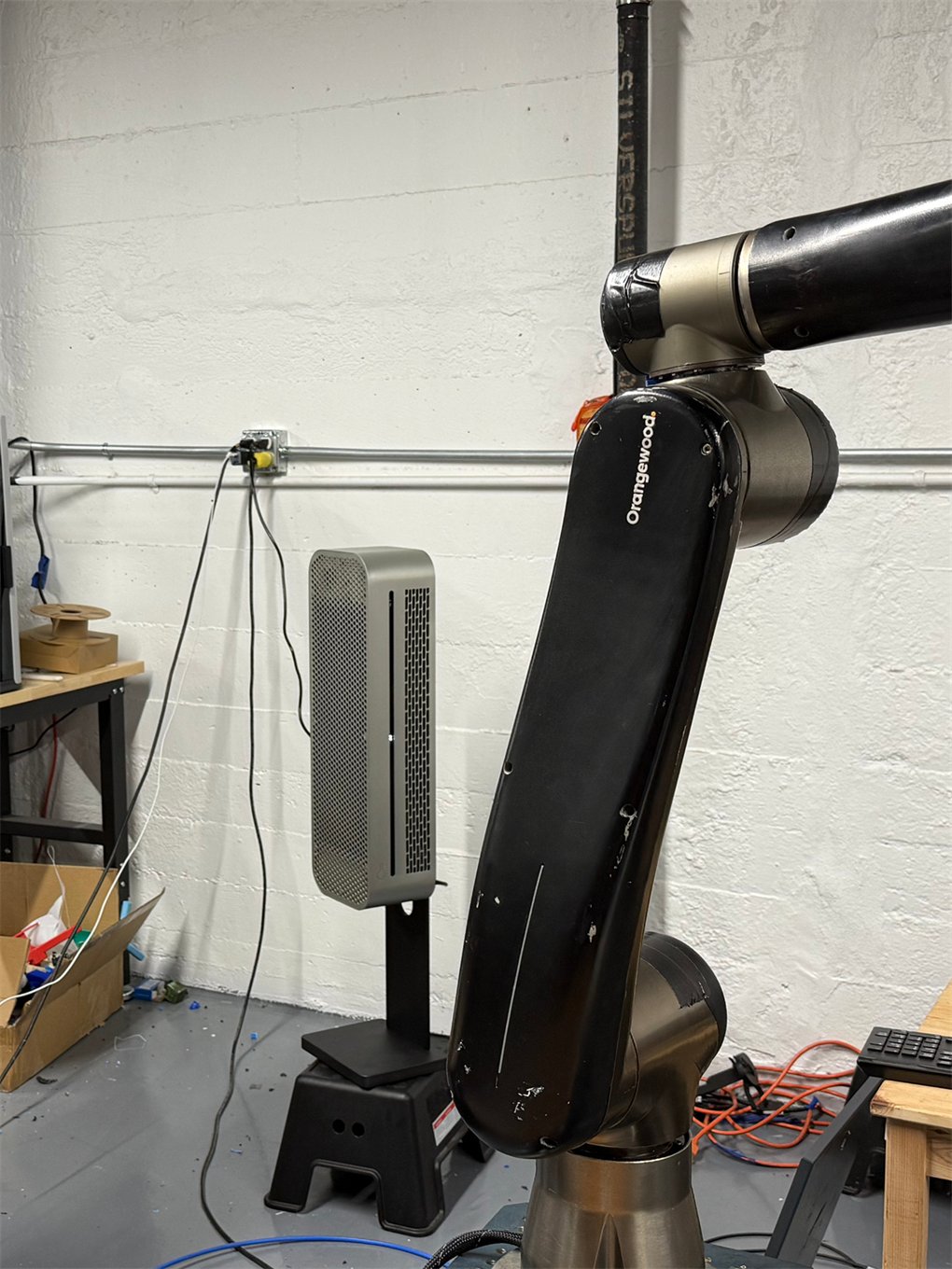 HIVE on its stand beside a robotic arm in a workshop